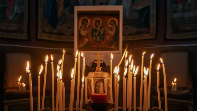 A lit candle in front of a painting of the Holy Trinity, evoking thoughts on "What Does It Mean If Lights Around You Flicker?