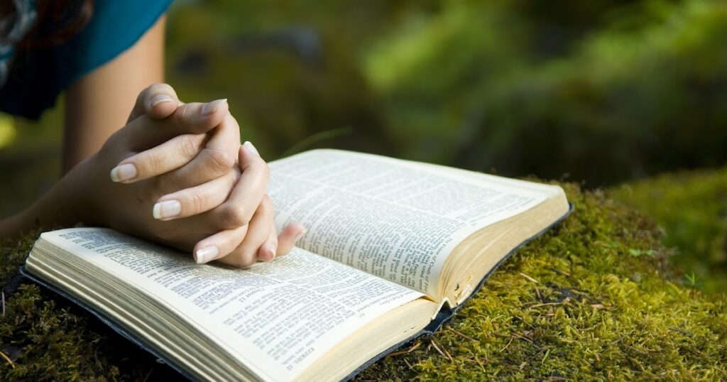 A woman's hands resting on a Bible, symbolizing prayer and reflection on the Butterfly Meaning in the Bible.