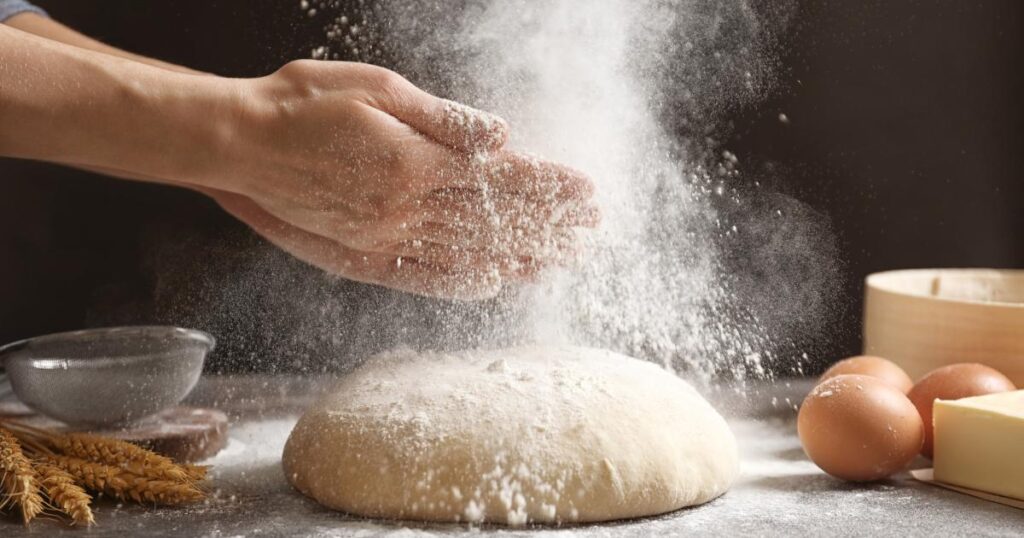 A person sprinkling flour on dough, preparing to create delicious Double Yolkers pastries.