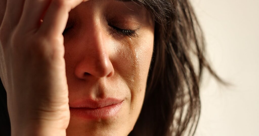 A woman holding her head in pain, reflecting on the meaning of dreams about cheating after a troubling experience.