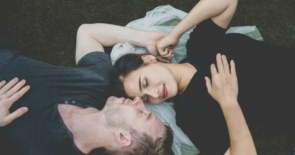 A couple laying on the grass, embodying the essence of dreams of love and relationships in a serene outdoor setting.